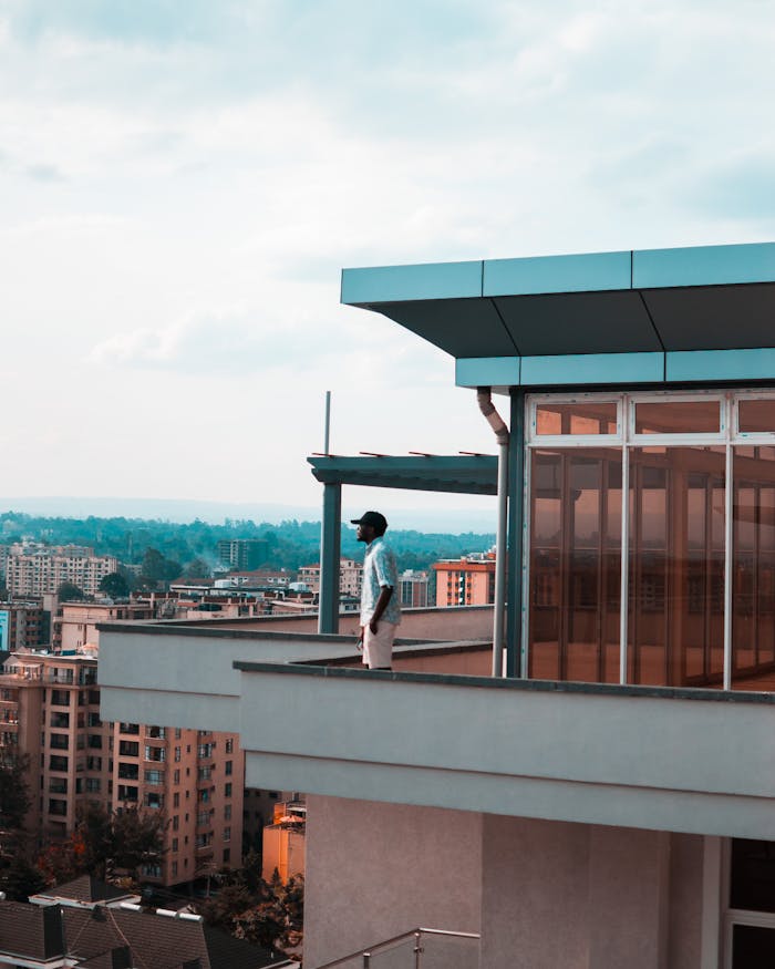 services-02 Man standing on a modern balcony overlooking a city skyline on a bright day.