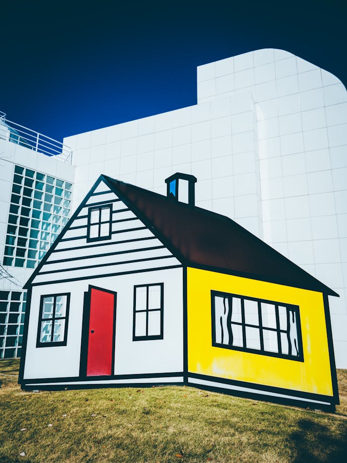 who-we-are Cartoon-style house sculpture against modern building facade on a sunny day.